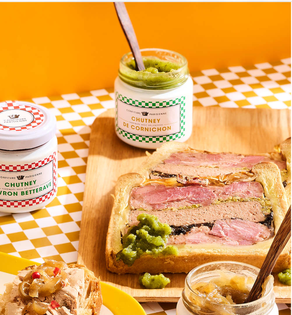 Pots de Chutney de Cornichon et Chutney Poivron Betterave près d'un pâté en croûte sur une nappe à carreaux jaunes