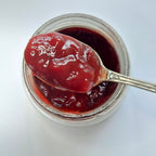 Cuillère en argent chargée de confiture rouge brillante au-dessus d'un pot ouvert, vue de dessus