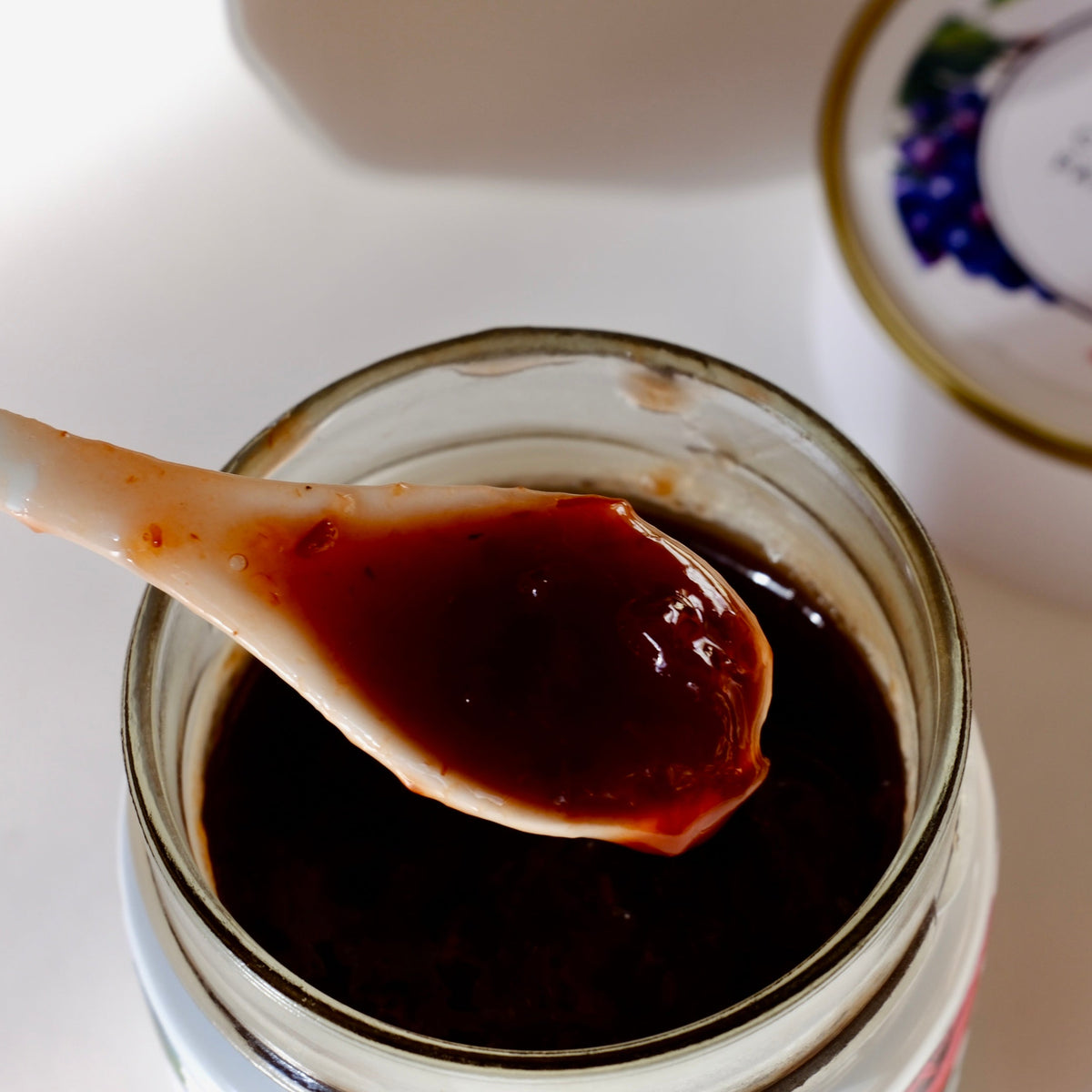 Cuillère en bois soulevant une confiture rouge sombre au-dessus d'un pot en verre ouvert