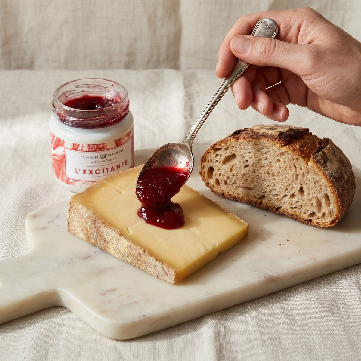 Confiture L'Excitante x Fabien Vallos déposée à la cuillère sur une tranche de fromage, pain de campagne à côté