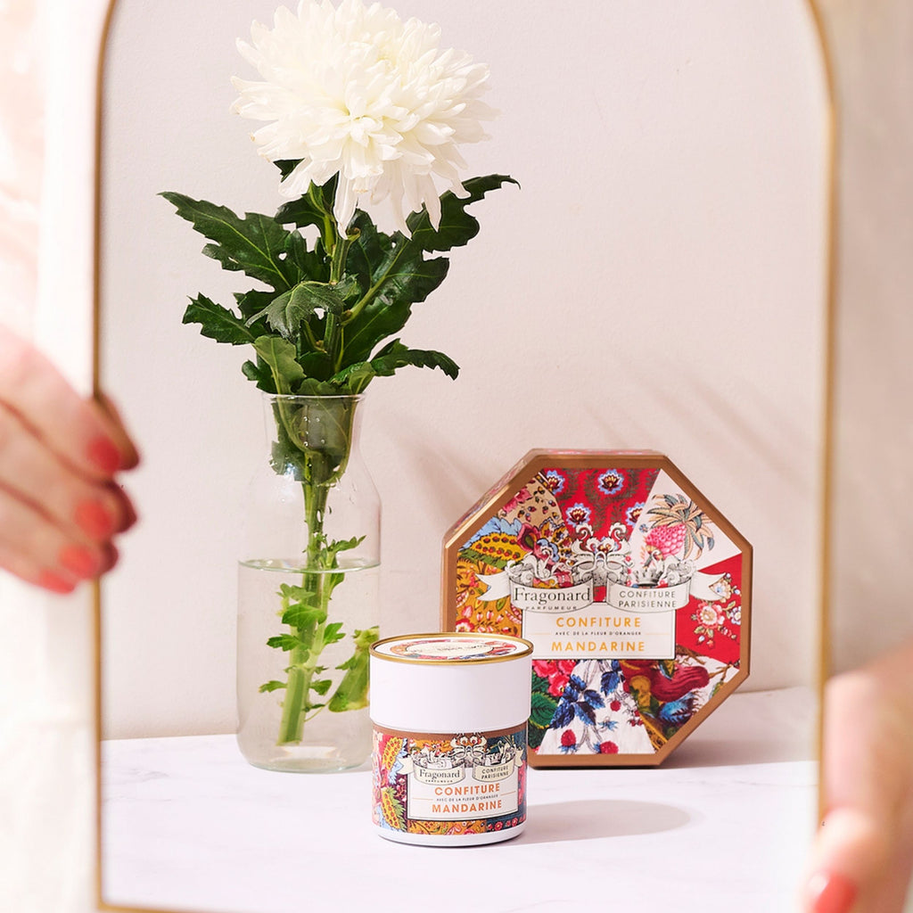 Pot et coffret octogonal Mandarine Fleur d'Oranger x Fragonard près d'un vase de fleurs blanches, miroir doré