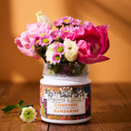 Pot vide Mandarine Fleur d'Oranger x Fragonard réutilisé en vase avec un bouquet de fleurs roses sur une table en bois