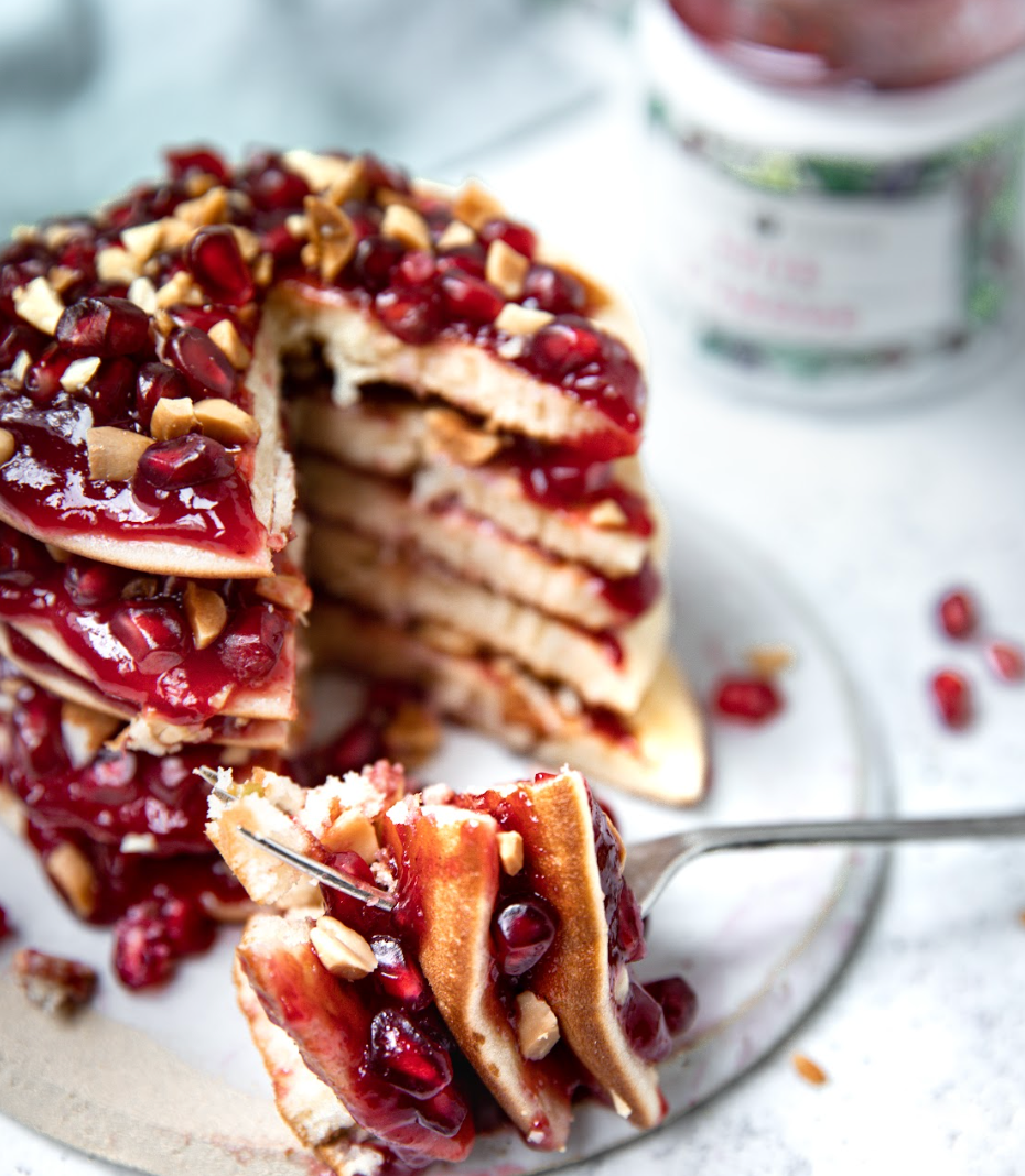 Pile de pancakes nappés de confiture rouge et de grains de grenade, un pot de confiture en arrière-plan