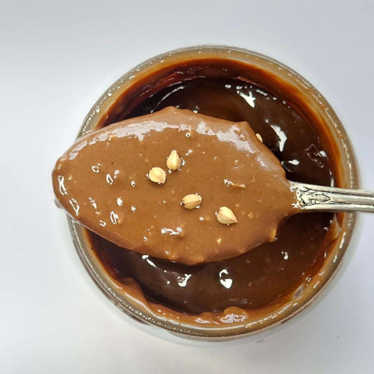 Cuillère en argent nappée d'une pâte à tartiner au chocolat avec éclats de noisette au-dessus d'un pot ouvert