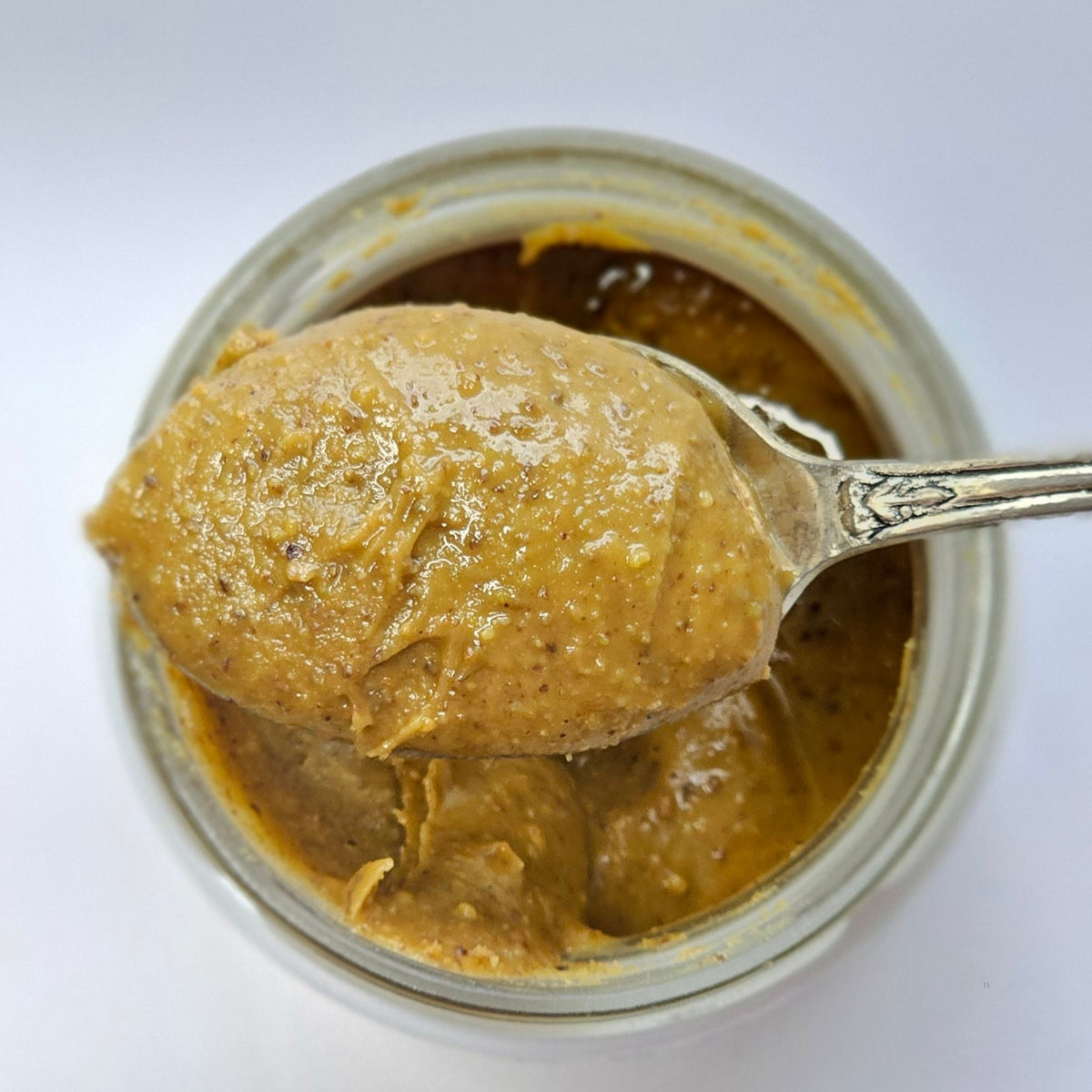 Cuillère en argent soulevant une pâte à tartiner noisette au-dessus d'un pot ouvert, vue de dessus